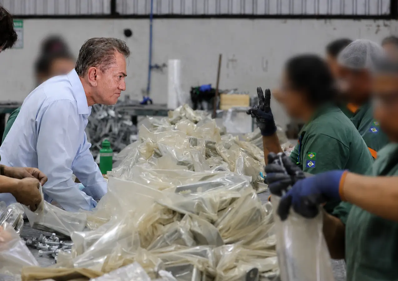 Foto que mostra o desembargador Orlando Perri, de camisa azul, conversando com reeducandas durante atividade de trabalho em uma linha de produção industrial.