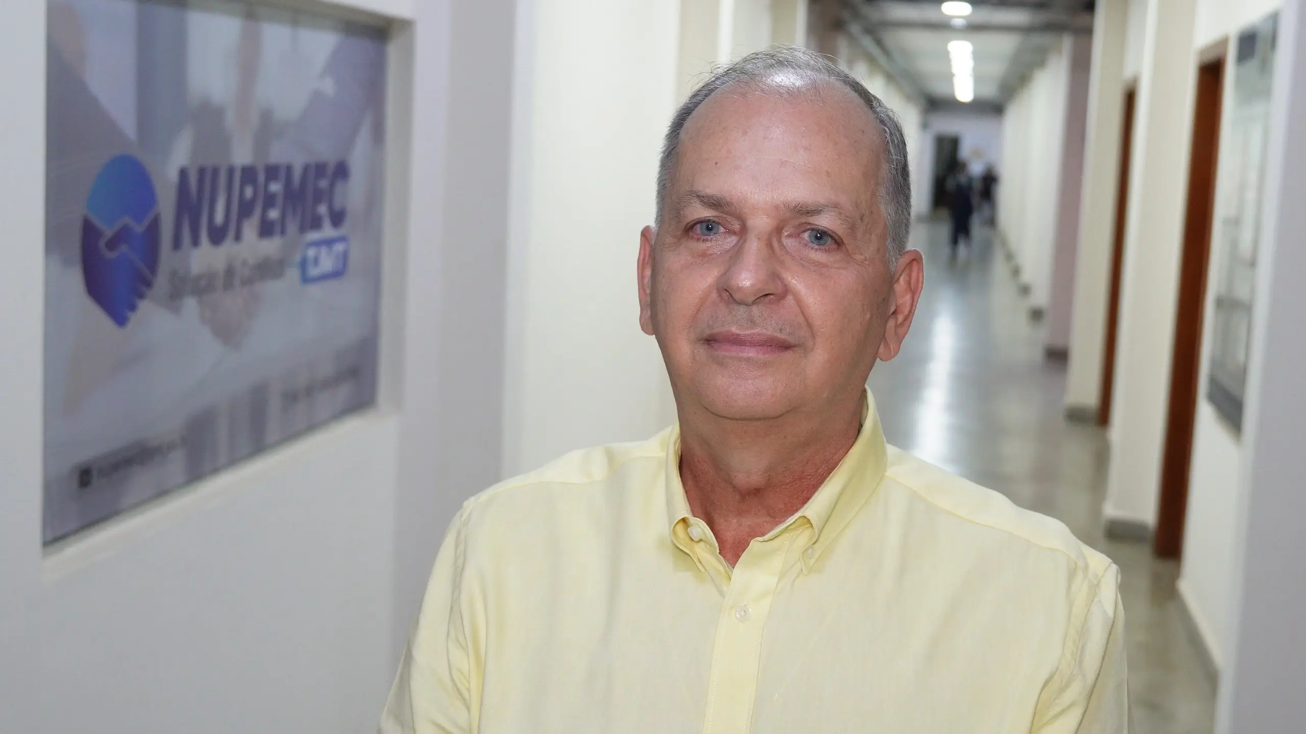 O gestor administrativo do Daje, Gláucio Corrêa é um homem de pele clara, cabelos curtos grisalhos, veste camisa social amarela de mangas longas. Ele está em um corredor, ao fundo há uma placa de identificação do Nupemec.