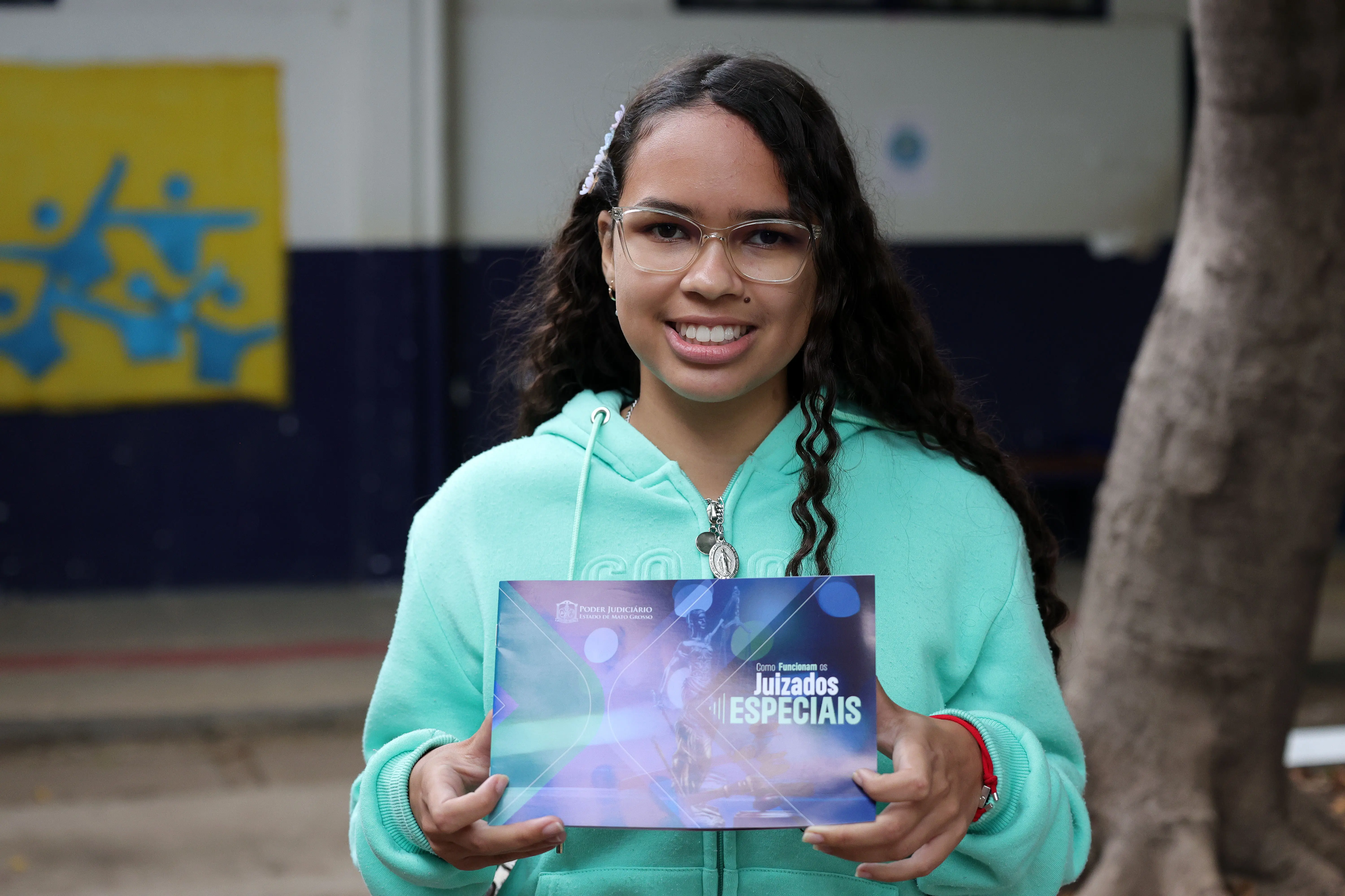 Estudante Nathália é uma jovem negra de óculos e moletom verde, segura o folheto 