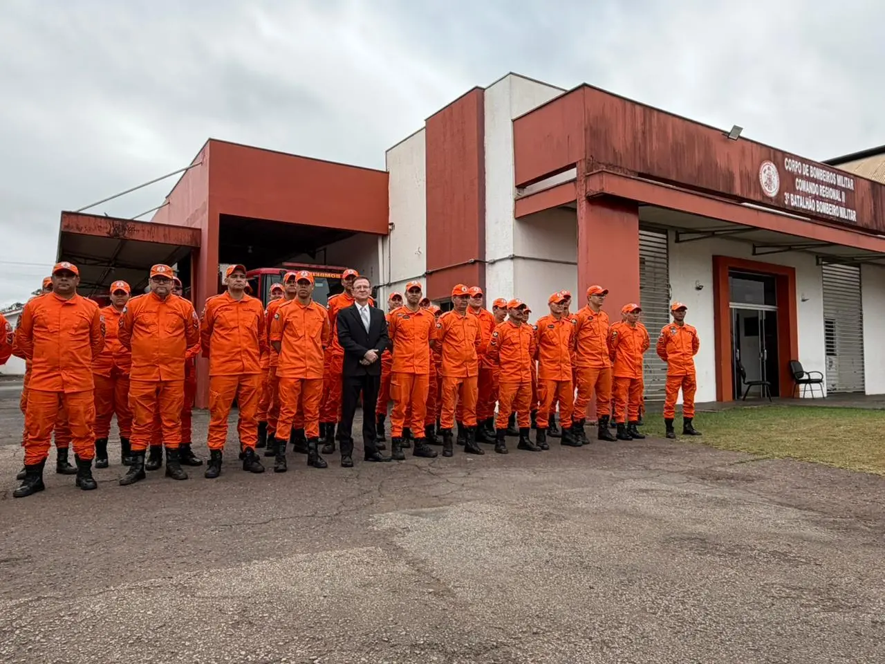 Bombeiros de uniforme laranja perfilados em frente ao quartel 