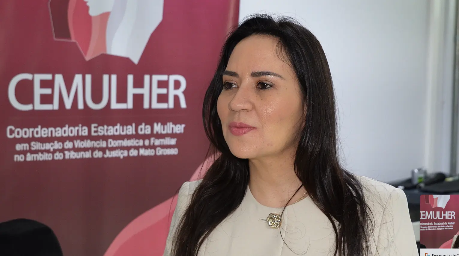 Juíza Tatyana Lopes  tem cabelos pretos longos, veste blusa bege clara com um broche dourado. Ao fundo, à esquerda, vê-se um banner vermelho com a palavra 