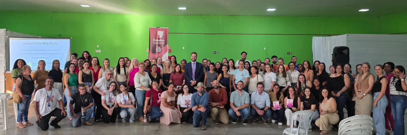 Foto de um grupo grande de pessoas. Ao fundo uma parede verde.